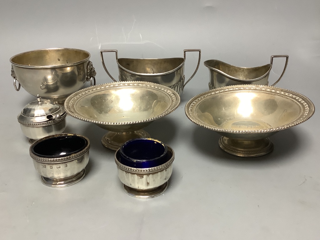 A pair of George V silver pedestal nut dishes, a small silver bowl with lion mask handles, a silver cream and sugar and a three piece silver condiment set